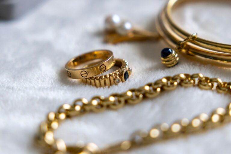 Verschiedene goldfarbene Ringe, Armbänder und Ketten auf einer hellen Unterlage